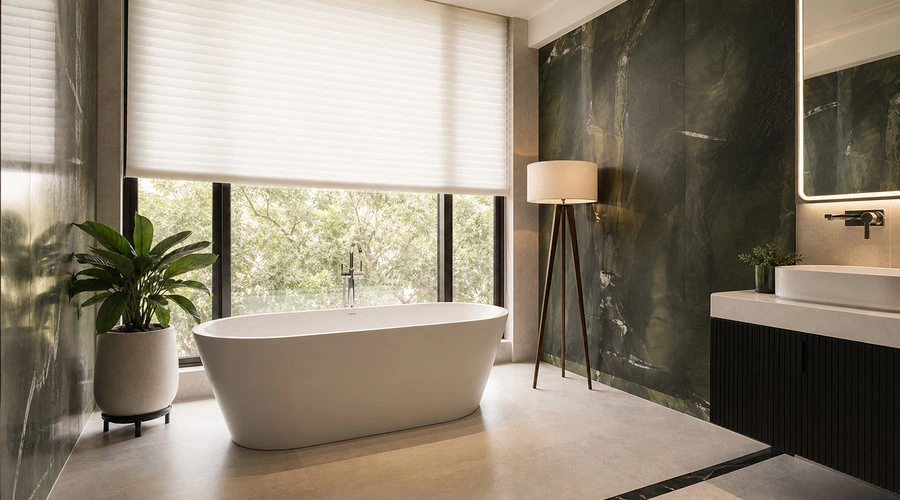 Green stone bathroom with freestanding bathtub beside a window